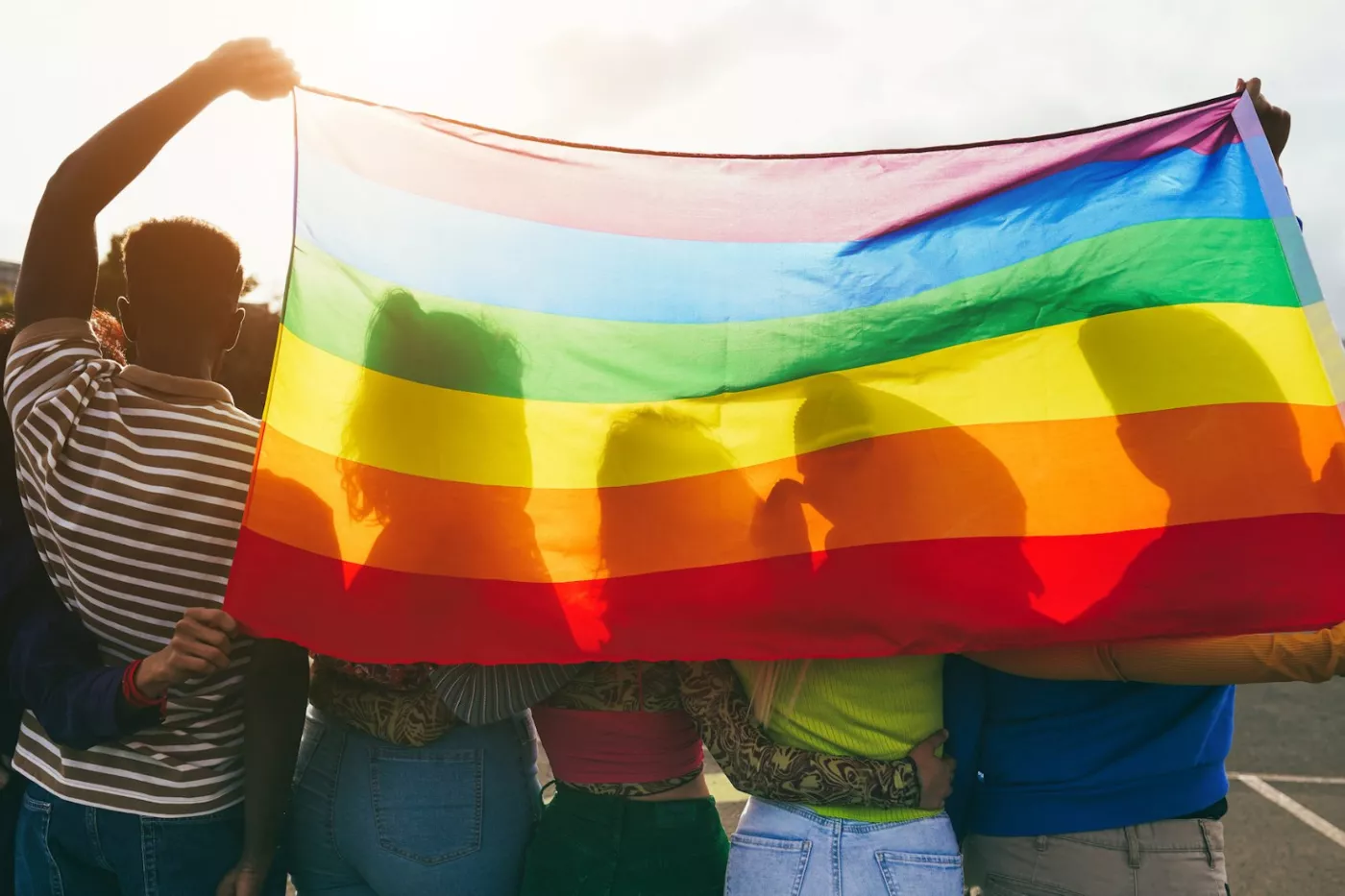 A group of people stand holding the traditional PRIDE flag.