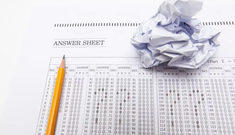 A pencil sits on a standardized test next to a crumpled piece of paper.