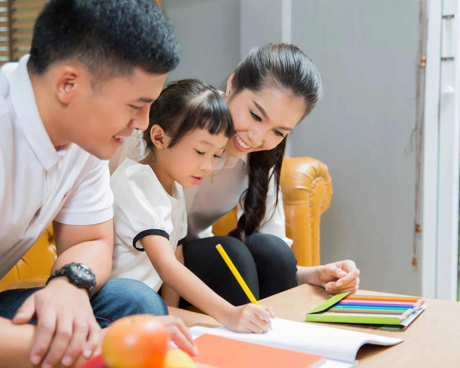 A mother and father help a child write.