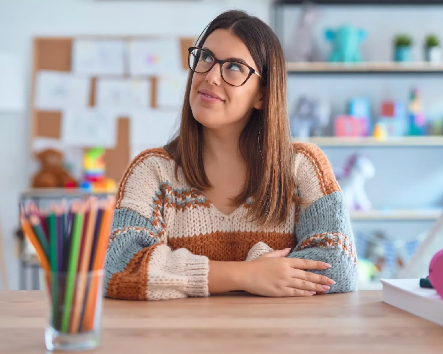 A teacher sits smiling to herself at her desk.