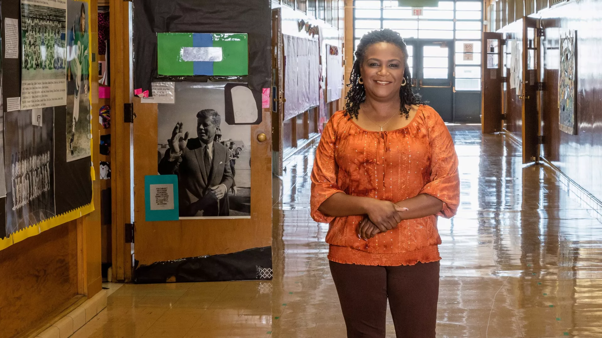 A teacher stands smiling in the school hallway.