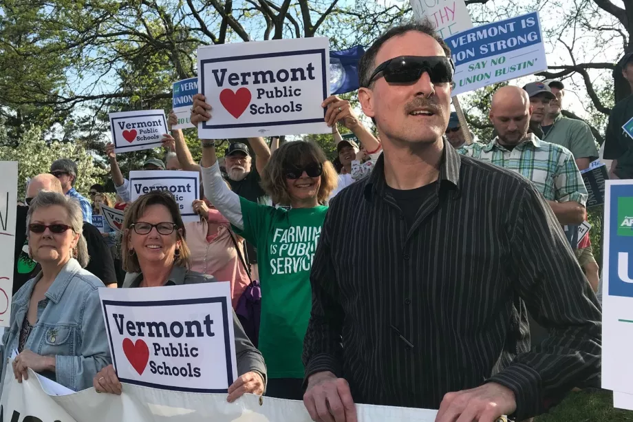 A group of Vermont educators stand with signs that say "Vermont (hearts) Public Schools"