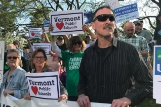 A group of Vermont educators stand with signs that say "Vermont (hearts) Public Schools"